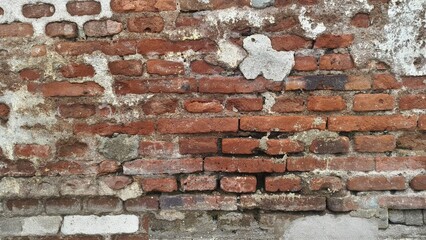 Obraz premium Old damaged red brick wall with cracked plaster and rough texture, showing weathered surface and rustic architectural detail.