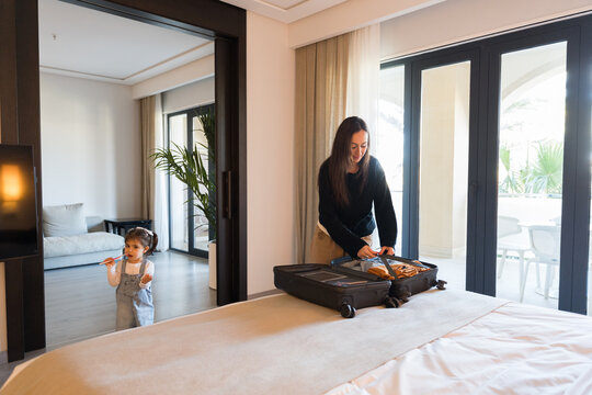 Mother unpacking suitcase in hotel room while daughter is playing