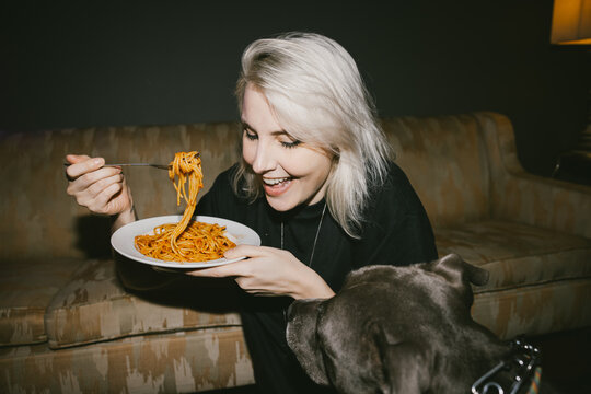 Woman Enjoying Pasta with Dog Watching