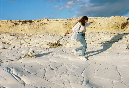 Woman running with a dog on a sandy coastal landscape during sunset