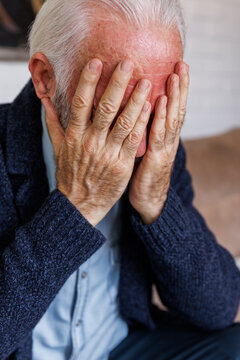 Senior man sitting with hands covering eyes