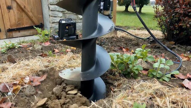 Detailed 4K Ultra HD construction close up view of a large auger drill bit boring deep into the ground showing the process of actively preparing the soil for hedge planting in a private garden area