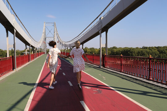 two women walking on a bridge by the river