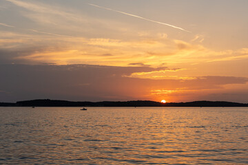 Fototapeta premium Lone fishing boat silhouette sailing on calm adriatic sea at breathtaking orange sunset and dark island coastline. Concept of solitude, simple life and timeless maritime beauty.