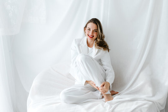 Young woman wearing white suit smiling and relaxing on white sheets
