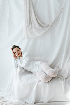 Young ballerina resting on white sheets in total white outfit 