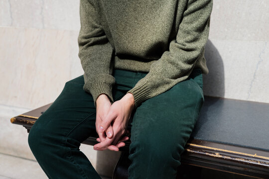 Anonymous man sitting on indoor bench with hands clasped