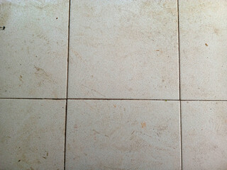 Close up of six dirty light beige floor tiles with grout lines and scattered dirt and scuff marks