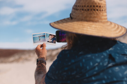 Man taking smartphone pictures of polaroids on a beach