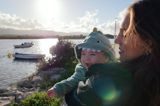 Mother holding baby wearing dinosaur costume by the river
