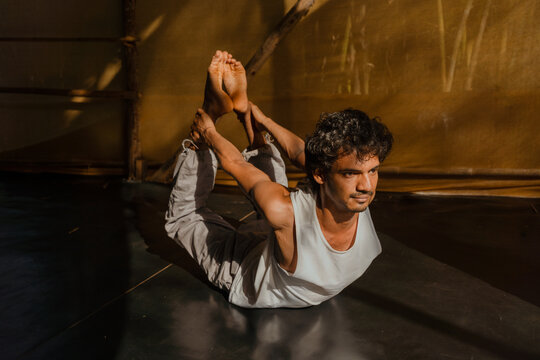 Focused Man Holding Bow Pose Dhanurasana in Studio Light
