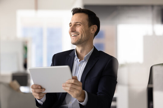 Smiling Hispanic office worker corporate employee holding digital tablet at workplace enjoying good news from marketing report satisfied with project success reviewing positive client feedback online