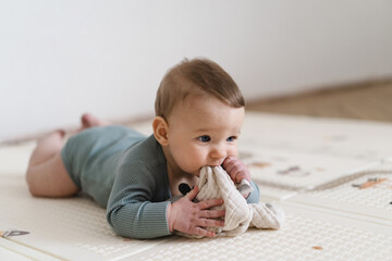 Obraz premium Adorable baby lying on tummy on a soft play mat and playing with a sensory toy. The infant is focused and curious while exploring the toy, supporting early learning and motor skill development.