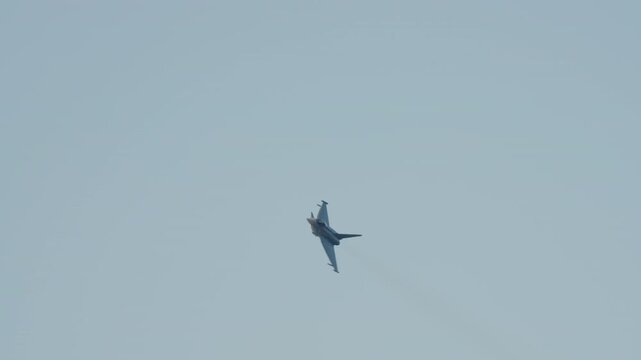 LUQA, MALTA - SEPTEMBER 28, 2025: A Eurofighter Typhoon fighter jet performs high-speed aerial maneuvers in a clear blue sky. The aircraft banks, rolls, and ignites its afterburners, leaving a short