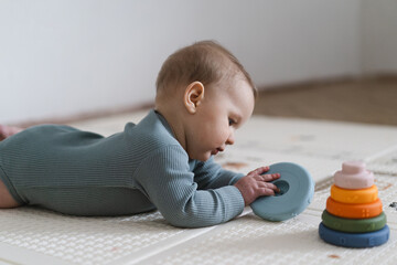 Adorable baby lying on tummy on a soft play mat and playing with a sensory toy. The infant is...