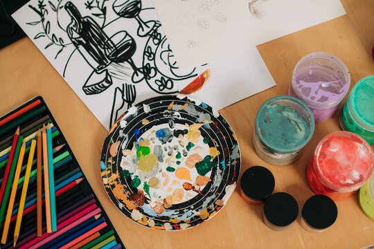 Paint palette, colored pencils and sketches on wooden desk