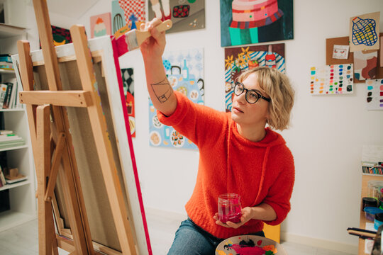 Woman painting with bright pink on canvas in home art studio
