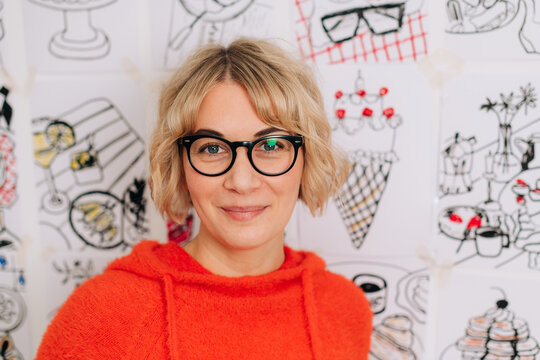 Portrait of female artist in front of her sketches on the wall