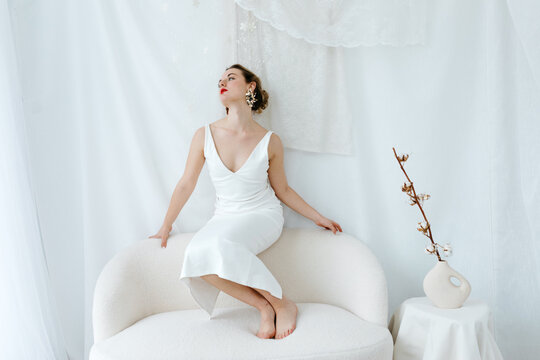 Elegant model posing on white sofa in minimalist studio
