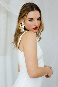 Woman with gold earrings and white dress posing in studio
