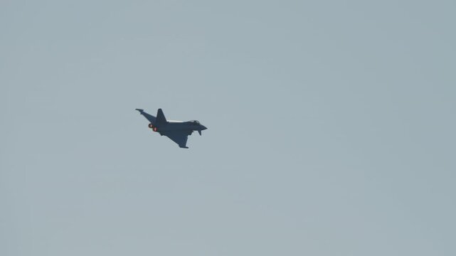LUQA, MALTA - SEPTEMBER 28, 2025: A Eurofighter Typhoon jet performs high-speed aerobatic maneuvers against a clear sky. Its afterburners glow as it climbs and turns, then it deploys flares during a