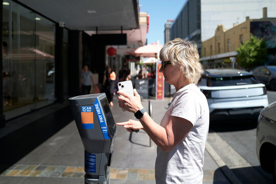 Woman using mobile payment at parking meter in city of Adelaide 