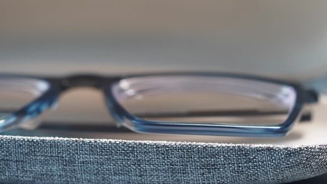 Macro shot of stylish blue eyeglasses resting inside open grey fabric protective case on dark surface