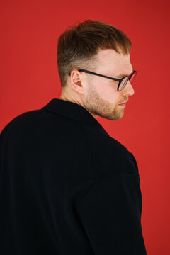 Stylish Man in Black Jacket and Glasses on Red Background