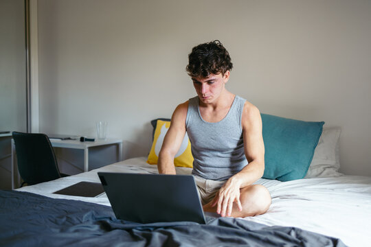 Student using laptop sitting on bed