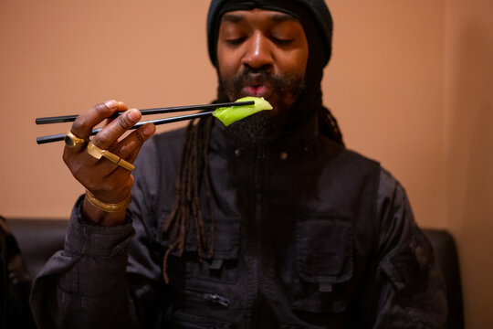 Black man eating pak choi with chopsticks