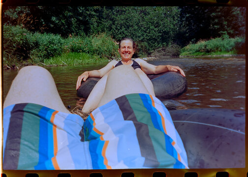 Degraded film photo of couple tubing on river 