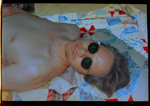 Man with sunglasses lays on beach blanket.