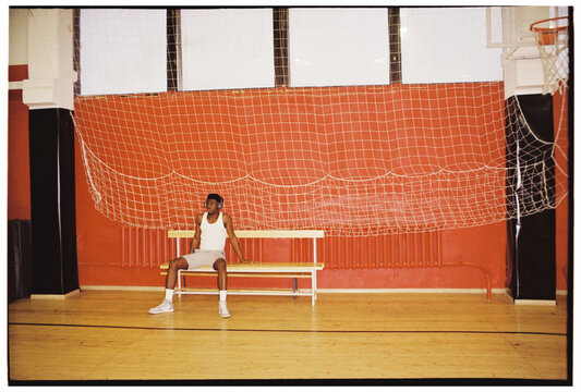 Basketball Player Resting on Bench in Gym

