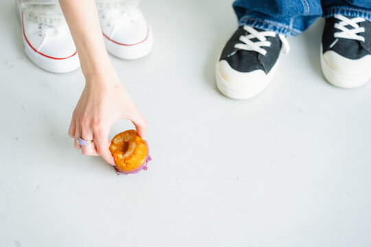The donut is lying on the floor near the feet of two people