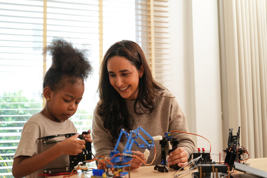 Happy mother looking at her young daughter with pride while assembling a DIY robotics kit together. Concept of STEM education, child development, and family bonding.