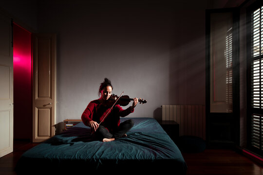 Happy woman playing violin at cinematic bedroom