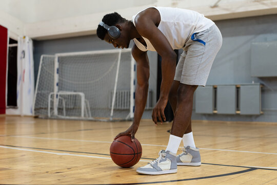  A young male basketball player bends down to pick up a ball in gym