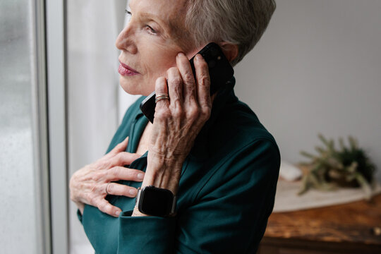 Senior Woman Talking on Phone While Standing by a Window