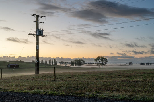 Foggy sunrise over farmland with electrical transformer.