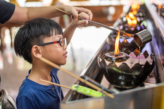 Boy lighting oil lamp with mother at Buddhist temple