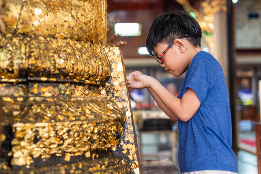 Boy placing gold leaf on statue at Thai temple