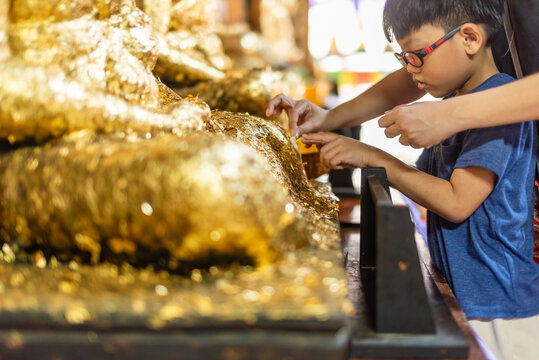 Boy applying gold leaf at Thai Buddhist temple