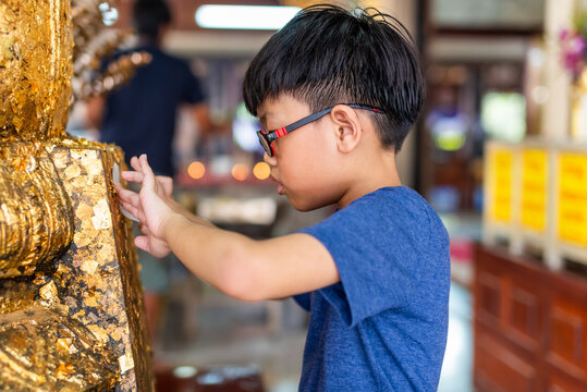 Boy placing gold leaf on statue at Thai temple