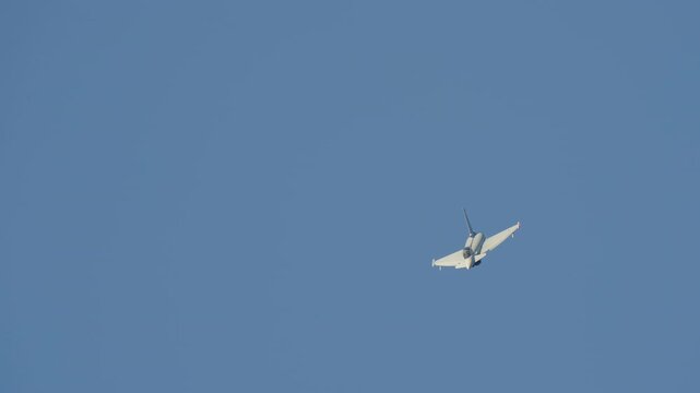 LUQA, MALTA - SEPTEMBER 28, 2025: A Eurofighter Typhoon fighter jet performs a slow-motion aerial maneuver, banking and turning against a clear, solid blue sky. A dynamic shot of military aviation
