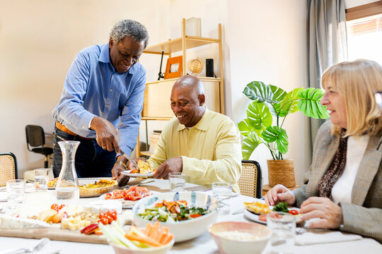 Host serving food to guest at senior friends reunion