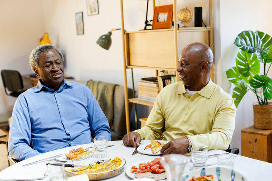 Male friends talking cheerfully by dining table checking smartphone