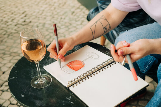 Anonymous woman drawing wine glass in sketchbook at cafe table