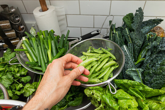 Point of view of a hand reaching towards fresh peas in colander