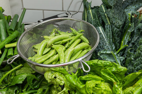 Green peas in a colander surrounded by greens