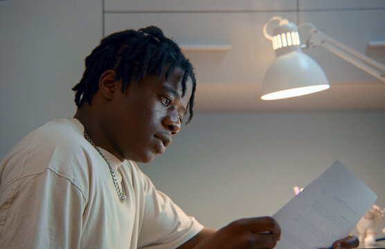 Focused student reading documents under desk lamp light